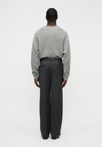 Γκρι πλεκτό πουλόβερ με υφασμένο σχέδιο καλωδίου στην πλάτη, συνδυασμένο με ψηλόμεσα, φαρδιά σκούρα γκρι παντελόνια.