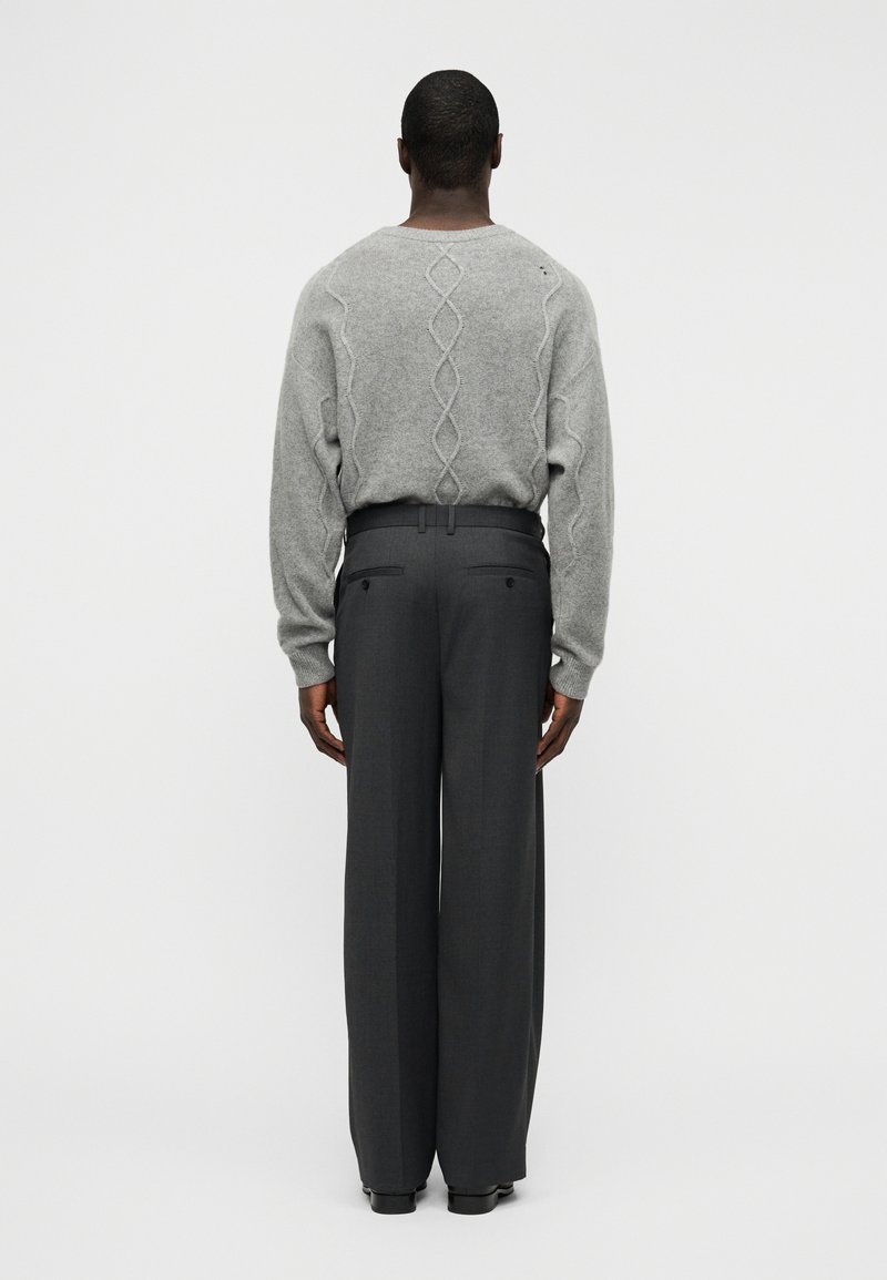 Pull gris en tricot avec un motif à torsades texturé dans le dos, associé à un pantalon gris foncé taille haute à jambes larges.