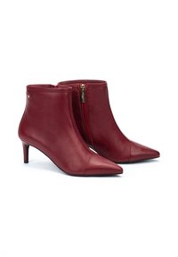 Botines de cuero rojo hasta el tobillo con punta afilada y tacón de aguja de 5 cm. Cuentan con un cierre lateral y una textura suave con acentos de hardware mínimos.