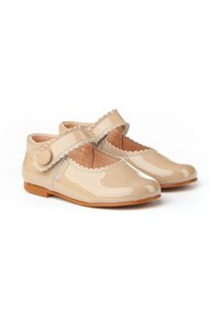 Zapatos beige patentados con bordes en forma de onda, una correa de Velcro y punta redonda; cuenta con un pequeño botón decorativo cerca de la correa.