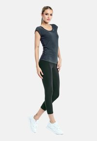 Dark gray short-sleeve athletic top paired with black capri leggings; model wears white sneakers; smooth textures, fitted design.