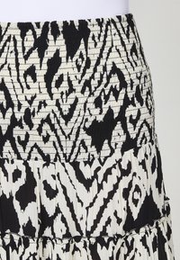 Jupe à volants noire et blanche en tissu texturé avec une taille smockée et un motif abstrait sur toute la surface.