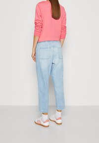 Rosa sweatshirt med långa ärmar, ljusblå löst sittande jeans, och vita sneakers med korallfärger och ljusgrå sulor.