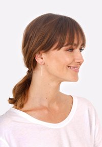 Pendientes de plata con un diseño de varilla delgada, que presentan un pequeño detalle de barra horizontal, llevados por una persona con cabello castaño de longitud media.