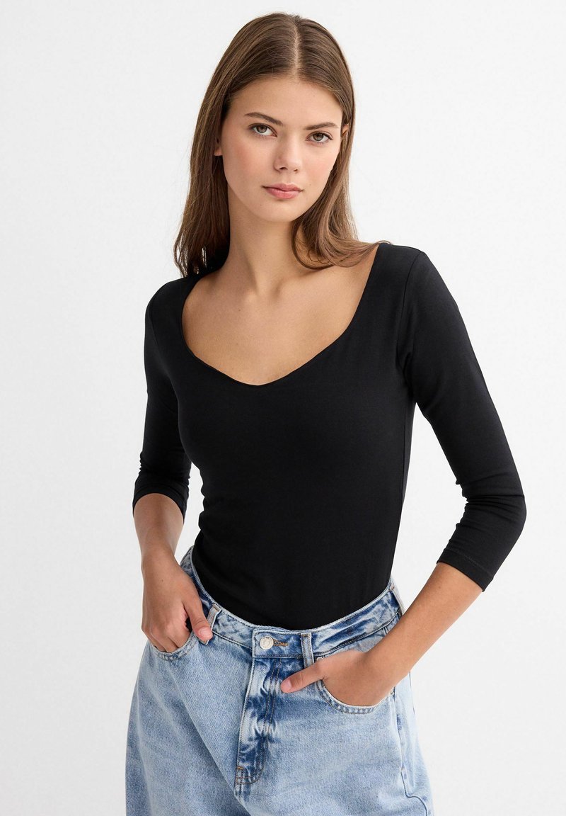 Top negro de manga larga con un escote amplio, diseño ajustado y material suave. Combinado con jeans de tiro alto de color azul claro con bolsillos.