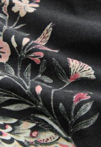 Tkanina w kwiatowy wzór na czarnym tle. Charakteryzuje się miękką fakturą, żywymi różowymi i zielonymi kwiatowymi detalami oraz plecionym wyglądem.