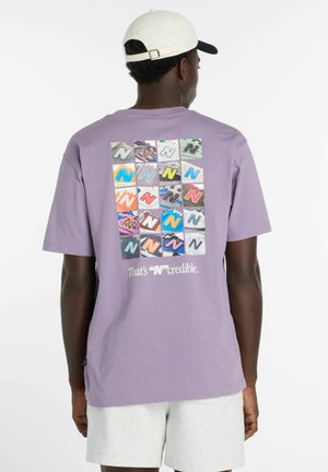 Mann trägt ein hellviolettes T-Shirt mit 20 bunten "N"-Logos in einem Raster und dem Text "That's 'N'credible" auf dem Rücken, weiße Kappe und helle Shorts.