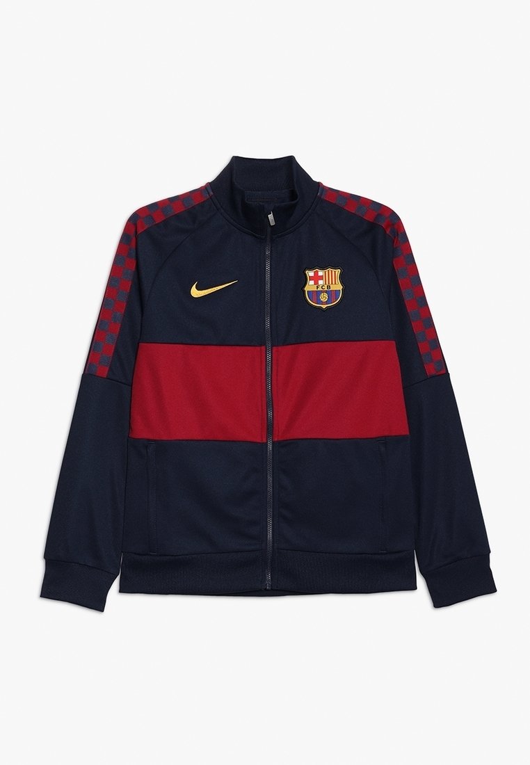 Navy ja punane Nike jakk, millel on lukuga eesmine osa, kõrge kaelus, kontrolltahvliga muster varrukatel ja Barcelona logo rinnal, valmistatud pehmest kangast.