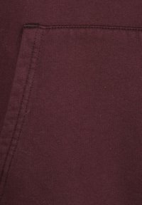 Bordeaux hoodie stof met een subtiele textuur, voorzien van een voorzak en stikdetails langs de randen. Zachte, katoenmix materiaal.