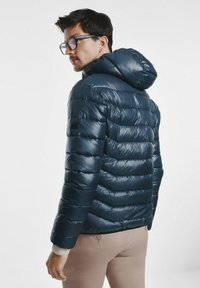 Granatowa puchowa kurtka z kapturem, z pikowanym wzorem, błyszczącą teksturą oraz elastycznymi mankietami. Na lewym boku widoczna jest naszywka z logo.