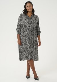 Vestido de estampado en blanco y negro con cuello con solapa, mangas largas, cintura elástica y cinturón de lazo en la cintura. Textura de tela suave.