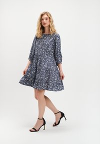 Sukienka w kwiatowy print w kolorze granatowym, z rękawami 3/4 i rozkloszowaną spódnicą. Połączona z czarnymi sandałami na obcasie. Gładka tekstura materiału.