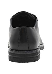 Chaussure en cuir noir avec un bout arrondi et une semelle plate. L'arrière présente une couture et un bord texturé sur la semelle.