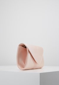 Pochette rose pâle en matériau lisse, avec une fermeture à rabat triangulaire, des bords arrondis et un éclat subtil à la surface.
