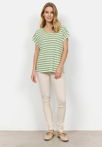 Grøn- og hvidstribet kortærmet top med V-hals, parret med lyse beige tætsiddende bukser og flade sko. Enkel design og afslappet pasform.