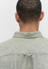 Groene, gestructureerde shirt gezien vanuit de achterkant. Het heeft een knoopsluiting kraag en een hanglus in het midden van de schouders.