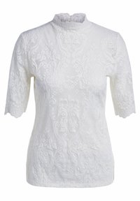 Blouse en dentelle blanche avec un col haut festonné et des manches courtes. Des motifs floraux et géométriques complexes sont visibles sur toute la surface.