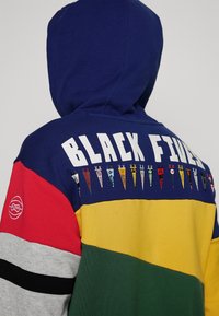 Felpa con cappuccio caratterizzata da un design multicolore con sezioni blu, rosse, gialle, verdi e grigie. Testo "BLACK FIVES" e bandierine decorative.