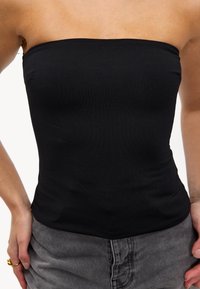 Haut noir sans bretelles en matériau extensible, au design ajusté, texture lisse, avec une finition unie et sans motifs ni accents visibles.