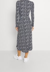 Svart långärmad klänning med vit och ljusblåt blommönster, midi-längd och utsvängd nederkant. Matchad med vita sneakers.