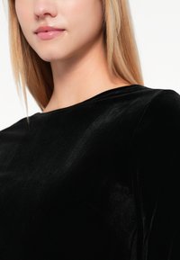 Vestido de terciopelo negro con un escote alto, textura suave y un ligero brillo, que resalta la rica y lujosa apariencia de la tela.