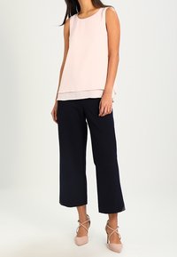 Haut sans manches rose pâle avec un design superposé, associé à un pantalon navy à jambes larges et à des ballerines roses claires à lacets. Tissu doux avec une coupe décontractée.