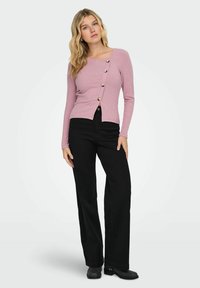 Jasnoróżowa, prążkowana bluzka z długim rękawem i kwadratowym dekoltem, ozdobiona guzikami z przodu, zestawiona z czarnymi spodniami o szerokich nogawkach i botkami za kostkę.