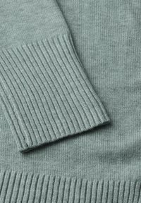 Světle zelený pletený svetr s žebrovanými manžetami a spodním lemem. Měkká textura s hladkým povrchem, zdůrazňující útulný design.