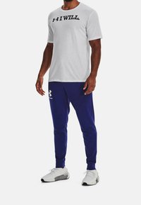 White short-sleeve t-shirt with "I WILL" text in black, paired with blue sweatpants featuring a white logo, completed with white athletic shoes.