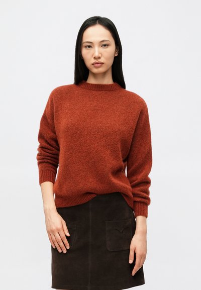 Pull tricoté couleur rouille avec un col rond et des poignets côtelés, associé à une jupe en suède foncé avec deux poches frontales.