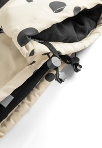 Tissu beige avec des pois noirs, présentant une fermeture éclair et des cordons de serrage ajustables avec des accents en forme d'étoile. Doublure noire douce visible à l'intérieur.