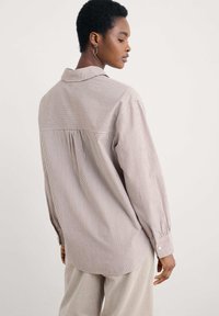 Camicia button-up a righe marrone e bianca, con colletto, maniche lunghe e dettaglio plissettato sulla schiena. Tessuto leggero, vestibilità rilassata.