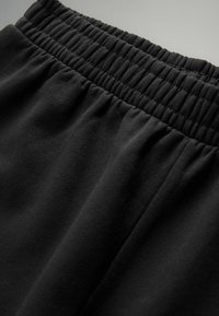 Pantaloni neri con vita elastica realizzati in tessuto morbido, con cuciture arricciate in vita e una superficie liscia in tutto il pantalone.