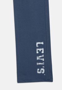 Jūras zila kokvilnas sporta bikses ar maigu tekstūru, ar balto drukāto "LEVI'S" logotipu vertikāli gar kreiso bikses kāju.