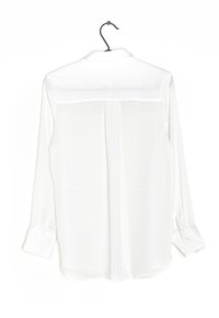 White long-sleeve shirt made of sheer fabric, featuring a back yoke, buttoned cuffs, and a straight hemline. Hangs from a black hook.