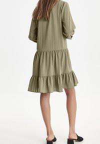 Oliwkowa sukienka do kolan z długimi bufkami, pionowymi paskami i warstwowym falbanianym dołem. Miękka tekstura oraz luźny krój.
