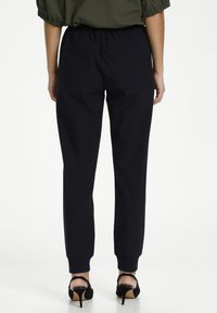 Marina joggingbyxor med elastisk midja, muddar och två bakfickor. Bärs med svarta klackar, vilket visar en elegant, avsmalnande design.