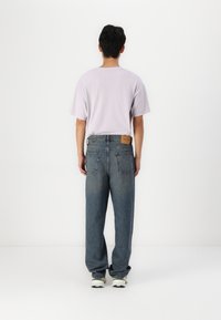 Lichtpaarse t-shirt met korte mouwen, gecombineerd met een losse spijkerbroek in middelblauw. De spijkerbroek heeft een leren label en twee achterzakken.