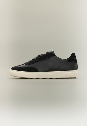 Niski czarny skórzany sneaker z czarnymi zamszowymi akcentami i lekko kredowobiałą gumową podeszwą, z wytłoczonym logo po boku i zapięciem na sznurowadła.