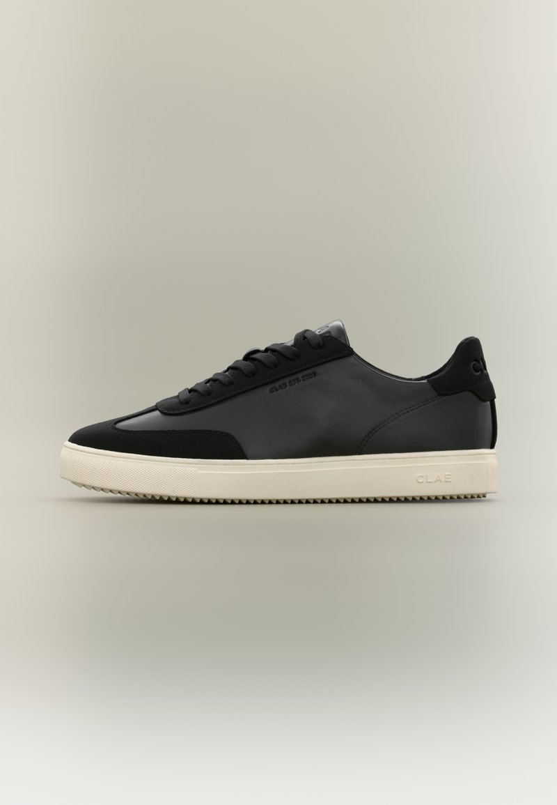 Baskets basses en cuir noir avec détails en daim noir, semelle en caoutchouc blanc cassé, logo embossé sur le côté et fermeture à lacets.