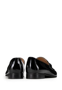 Zwarte gepatineerde leren loafers met een strak ontwerp, lage hak en een gladde textuur. Gedetailleerde stiksels langs de naden en geen zichtbare hardware.