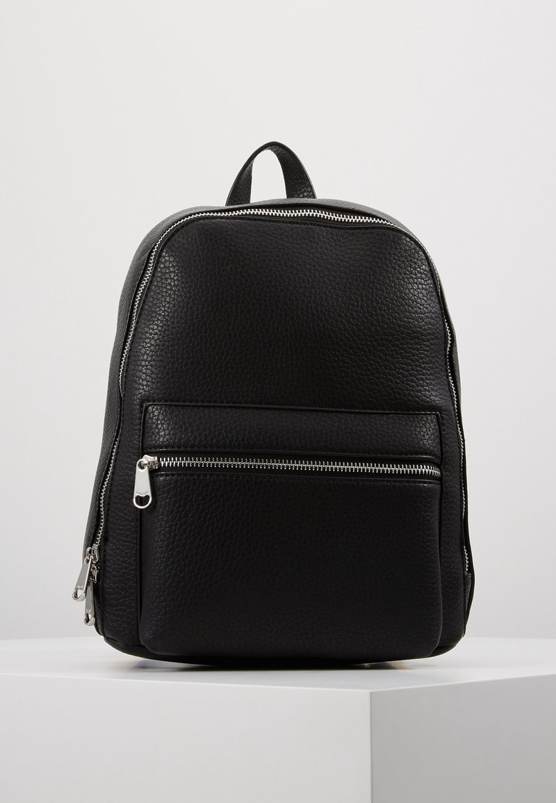 Sac à dos en cuir noir avec une finition texturée, doté d'une poche avant zippée, de détails de fermeture éclair argentés et d'une poignée de transport unique.