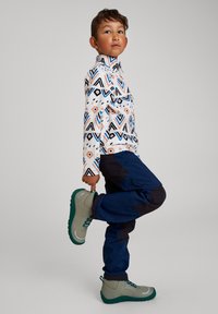 Camisa de manga larga con un patrón de formas geométricas en tonos azules, negros y melocotón; pantalones marinos; botas de senderismo grises y verdes.
