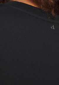 Sudadera negra de algodón con cuello acanalado. Logo sutil "ck" en plata cerca del cuello. Textura suave y diseño ajustado.