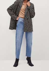 Płaszcz w czarno-białym wzorze w jodełkę, noszony na beżowej dzianinowej bluzce, w połączeniu z jasnoniebieskimi podartymi dżinsami i czarnymi botkami na obcasie.