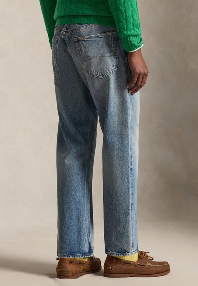 Άτομο που φοράει ανοιχτό μπλε τζιν κανονικής γραμμής, πράσινο πουλόβερ με πλέξη καλώδιο, κίτρινες κάλτσες και καφέ δερμάτινα μοκασίνια.