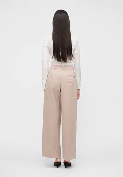 Φαρδιά παντελόνια σε ανοιχτό μπεζ με λεία υφή, ψηλή μέση και μία πίσω τσέπη, συνδυασμένα με εφαρμοστό λευκό μακρυμάνικο τοπ.
