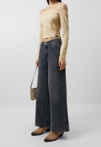 Beige off-shoulder toppi pitkällä hihalla yhdistettynä harmaisiin leveälahkeisiin farkkuihin. Sisältää pienen käsilaukun ja ruskeat korkokengät.