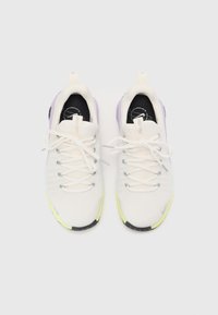 Witte athletic schoenen met een gestructureerde bovenkant, voorzien van paarse accenten, reflecterende veters en een felgele rubberen zool.