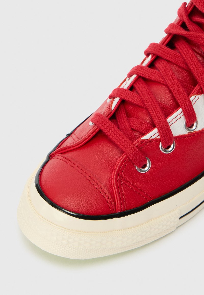 Sneaker in pelle rossa con punta rotonda, suola in gomma nera, dettagli in cucitura bianca e lacci rossi texture.